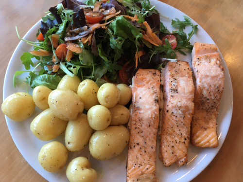 Oven roasted salmon, boiled potatoes, and a green salad on a white plate.
