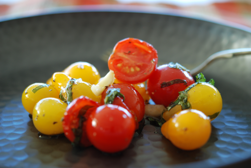 Yellow and red cherry tomatoes with basil and garlic and olive oil served on a dark grey dish