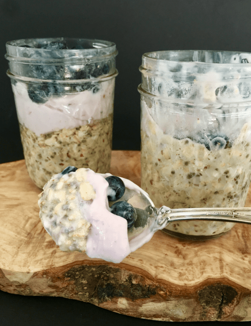 A close up of a spoon of overnight oats with two jars filled with overnight oats in the background