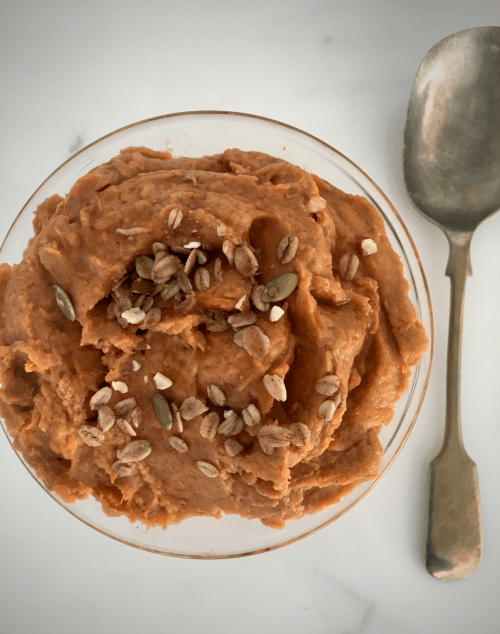 A bowl of homemade sweet potato casserole, topped with granola and maple syrup